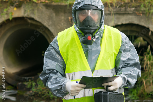 a man in a protective suit and mask holds a suitcase with equipment and a tablet in his hands to record research results