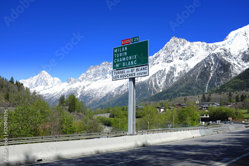 Road sign showing directions to Milan, Turin, Chamonix and Mont Blanc with snowy mountains in the background near Mont Blanc tunnel.