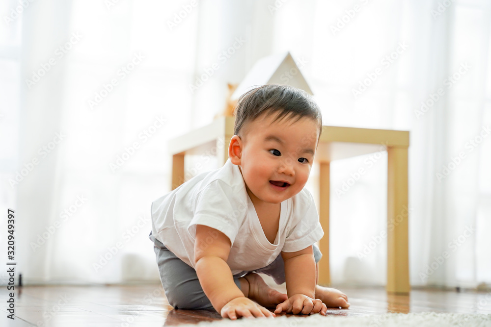 One lovely male infant laughing and having fun in living room against white windows. He can sit on the floor in living room at home. One lovely male infant laughing and having fun in living room against white windows. He can sit on the floor in living room at home.