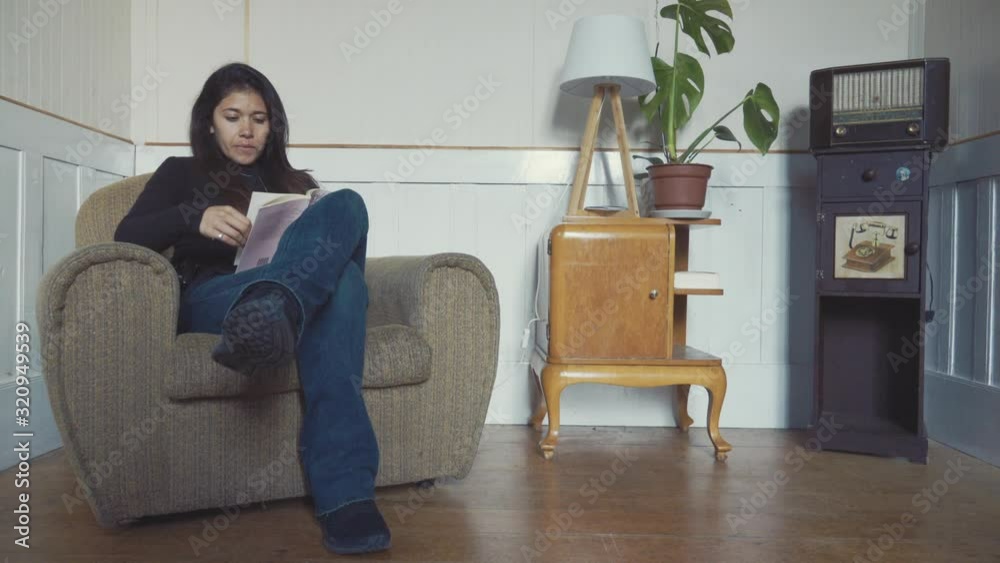 Hispanic woman reading in a small living room with vintage furniture. 4k Hispanic woman reading in a small living room with vintage furniture. 4k