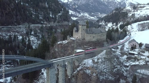 Flying with the drone over a castle and over a bridge, a train is crossing the bridge, The landscape looks like in winter wonderland. photo