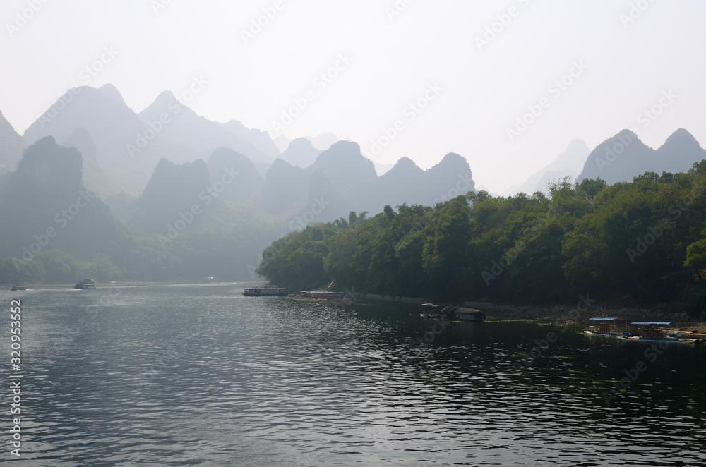 Tour boats on the Li River Guangxi China with karst dome mountains in the haze