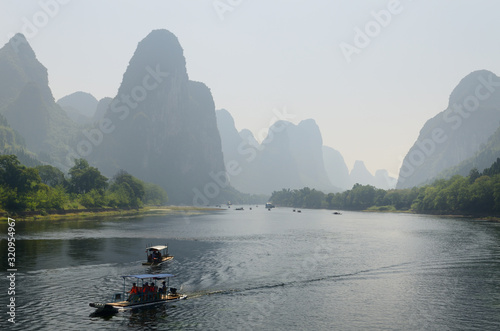 Tour boat rafts on the Li river Guangxi China with tall karst mountain peaks receding in the haze © Reimar