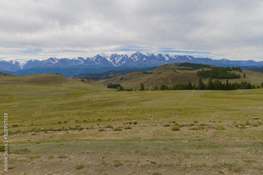 Panoramic view of a mountain valley summer, soft light, white clouds, blue sky. Altai mountains. Road, snow at the top