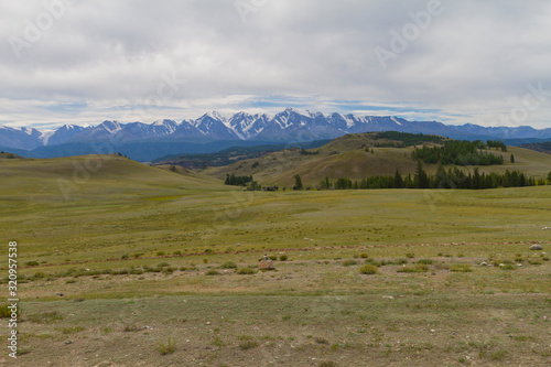 Panoramic view of a mountain valley summer, soft light, white clouds, blue sky. Altai mountains. Road, snow at the top