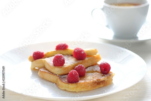 Two sweet toasts with raspberries sprinkled with sugar served on a white plate with tea in the background.