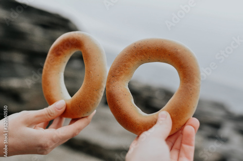 two bagels in the hands of two people, a light snack in the fresh air on the background of the sea