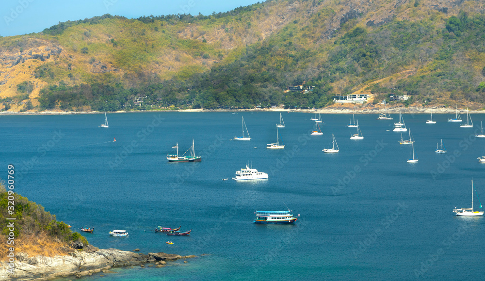 Obraz premium Many white boats and boats in the sea bay surrounded by rocks and islands, with hotels and houses on the banks of the green bank.