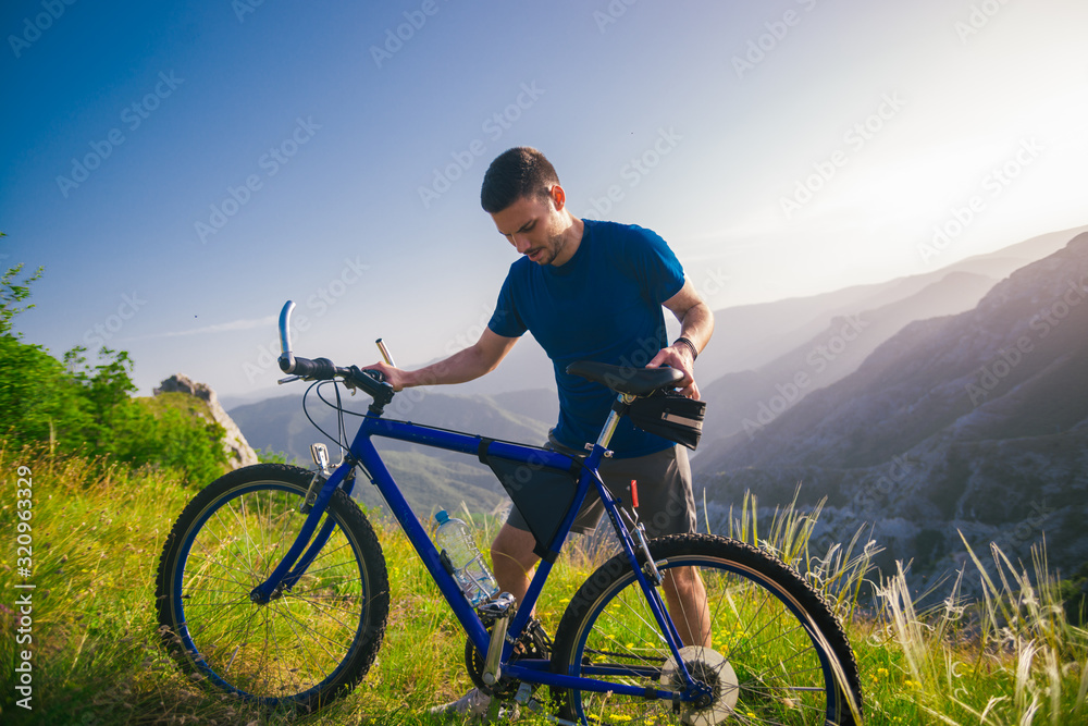 Perspective of a fit mountain biker pushing his bike uphill with amazing view on a forest, river and mountains in the background. Amazing green nature at sunset. Perspective of a fit mountain biker pushing his bike uphill with amazing view on a forest, river and mountains in the background. Amazing green nature at sunset.