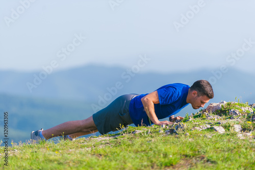 A young fit male athlete is doing push-ups outdoors on a cliff while looking at the breathtaking mountain line. © qunica.com