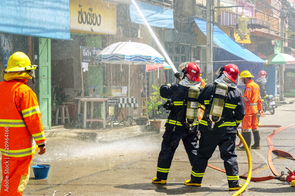 Obraz premium Firefighters of Lampang city confederate water spray and control the hoses to quench the fire in the real annual rehearsal fire drill in urban city.