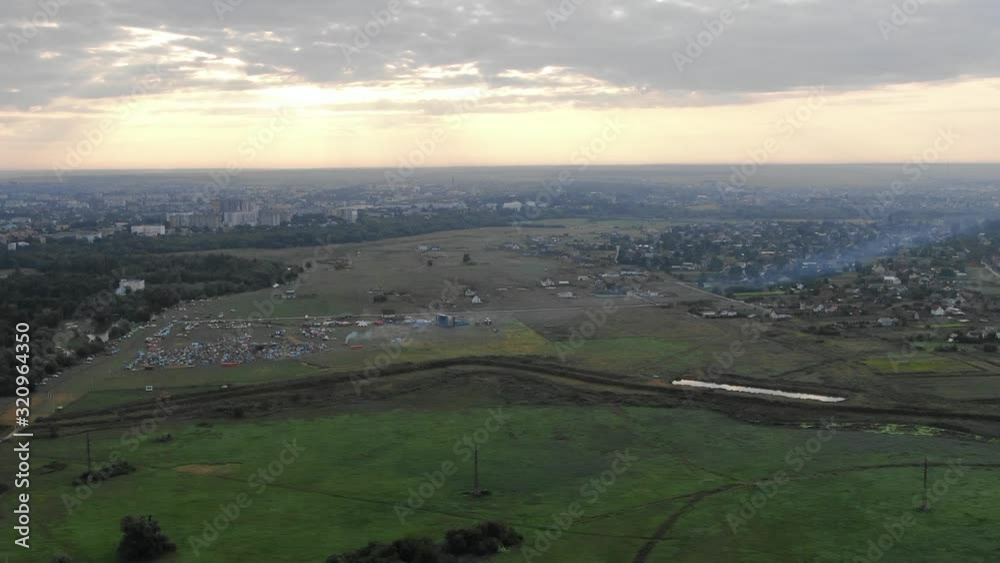 Aerial View Over Field in Eastern Europe During Music Festival With City in the Background Aerial View Over Field in Eastern Europe During Music Festival With City in the Background