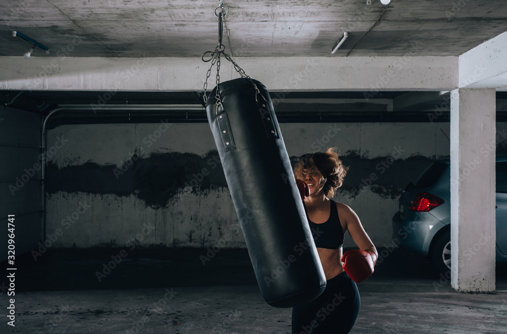 Strong young woman punching a boxing bag inside the garage