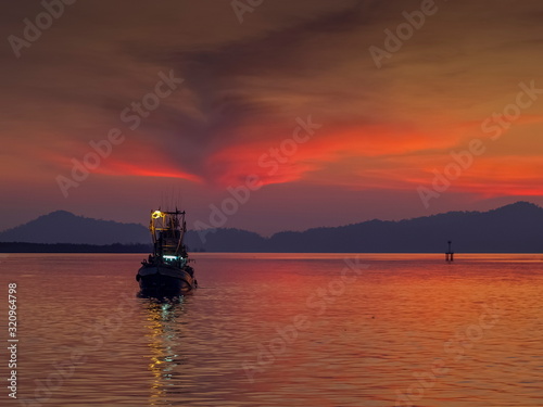 Sea view evening of fishing boat running in the sea with red sun light and cloudy sky background  twilight at Kuraburi Pier  Phang Nga  southern of Thailand.
