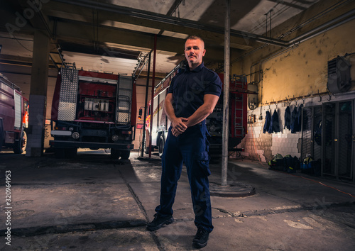 Portrait of handsome firefighter standing against trucks at fire station