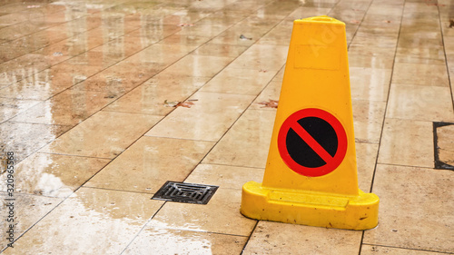 Yellow plastic cone with warning sign on slippery wet tile floor