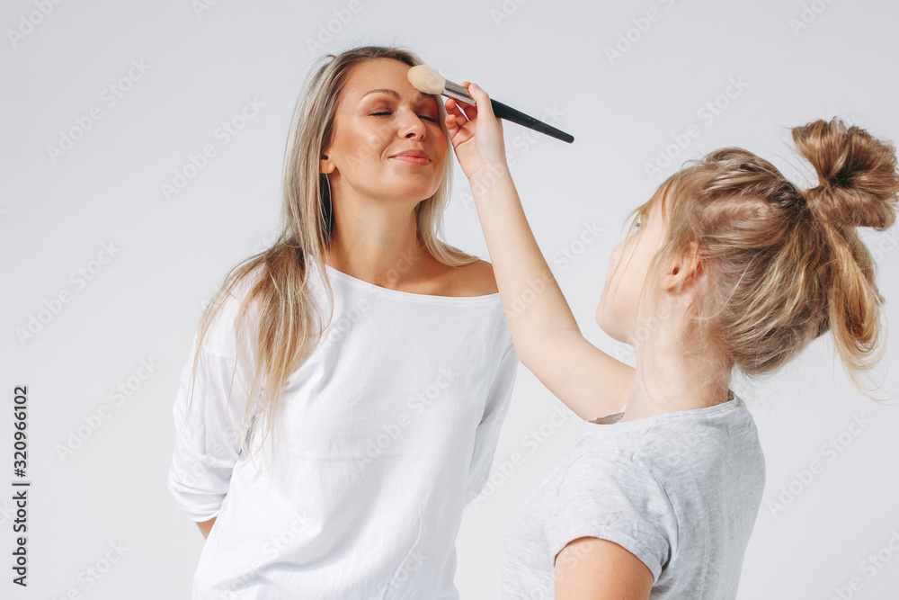 Obraz premium Young beautiful blonde mom and daughter in pajamas having fun together isolated on the white background, makeup girls party