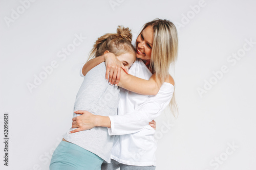 Beautiful blonde mom and daughter preteen in pajamas hugging and having fun isolated on white background