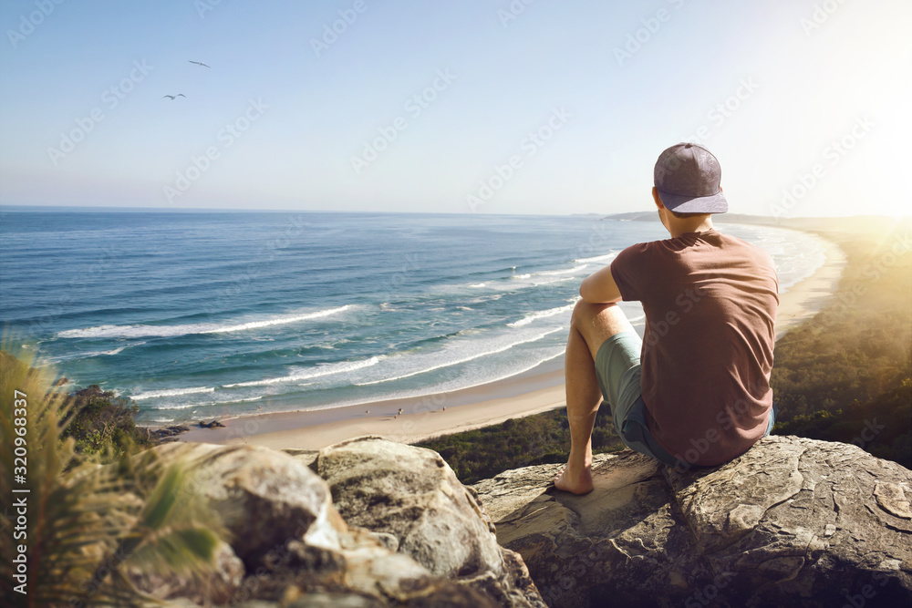 Young man sitting on a rock above a beautiful coastline