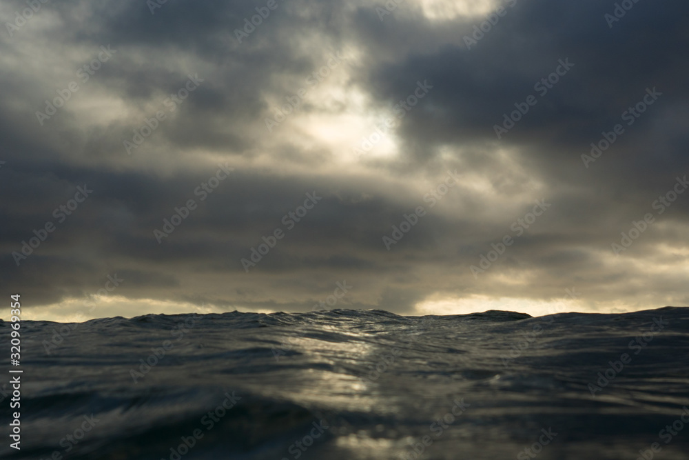 Close up on the surface of a dark sea in selective focus, with a moody cloudy dark sky behind.