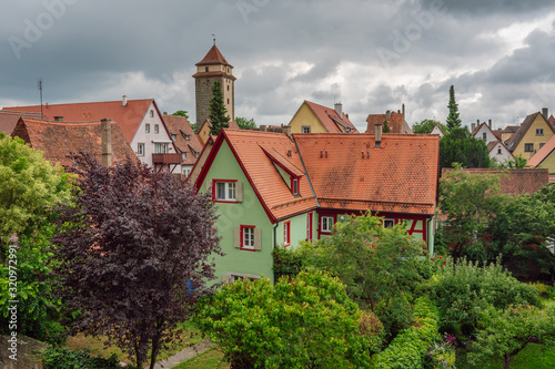 Beautiful old green house among green trees, roofs medieval city of Rothenburg ob der Tauber in the background, Bavaria, Germany.