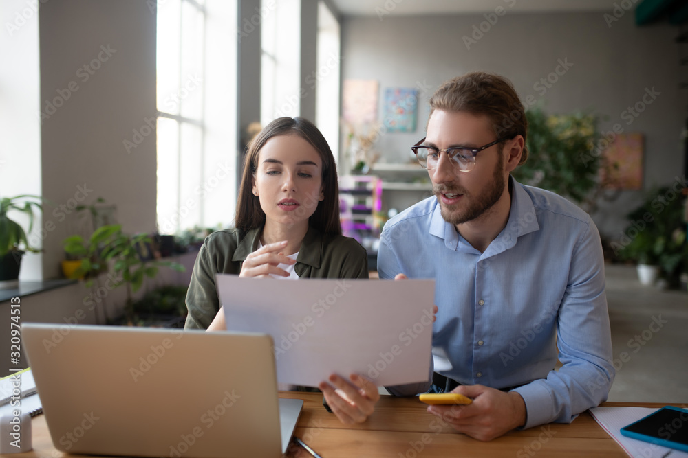 Girl and young man at the table familiarize themselves with project. Girl and young man at the table familiarize themselves with project.