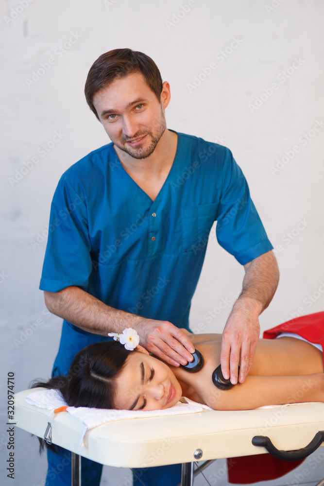 Obraz premium Young Asian woman enjoying the therapeutic effects of a traditional hot stone massage at luxury spa and wellness center