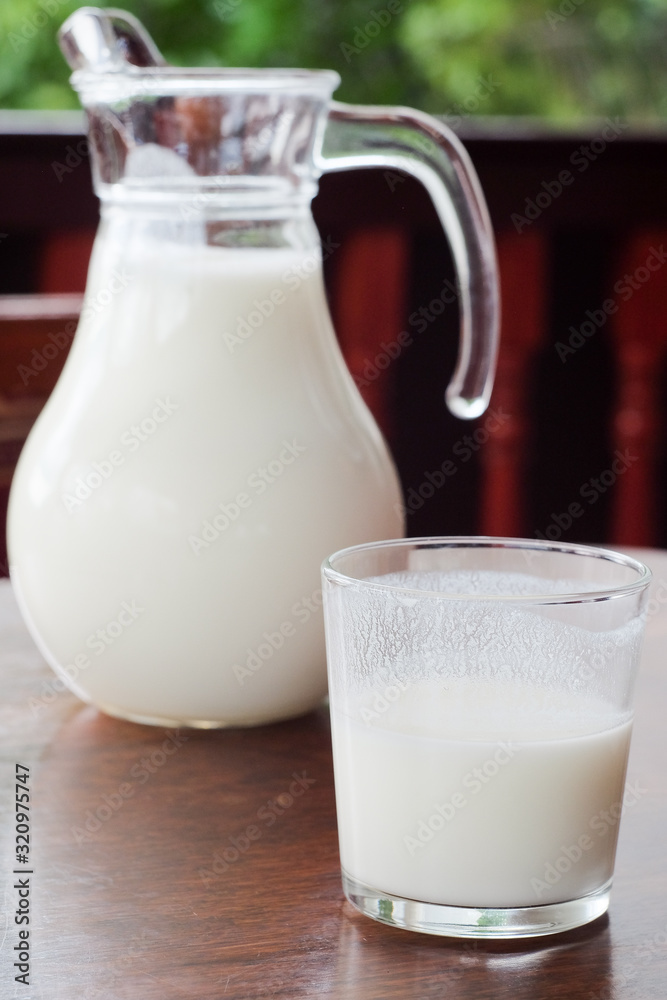 Close up glass of ayran with jug on the background. Traditional oriental turkic sour milk drink in the glass on the table. Kefir Close up glass of ayran with jug on the background. Traditional oriental turkic sour milk drink in the glass on the table. Kefir