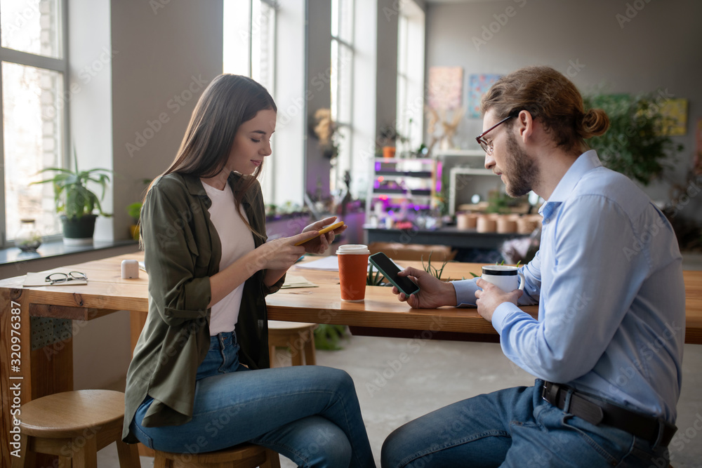 Girl and man with smartphones at a table in office.