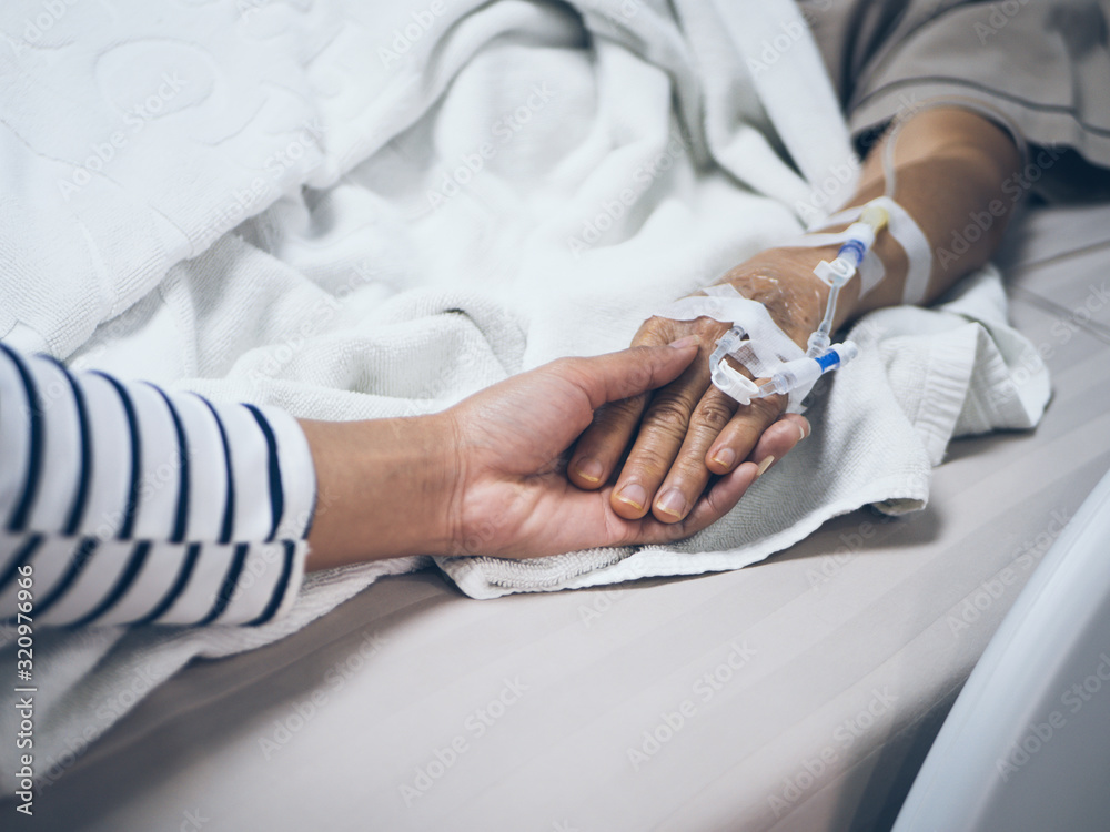Young woman hand hold old aged woman hand while lying in bed at hospital.