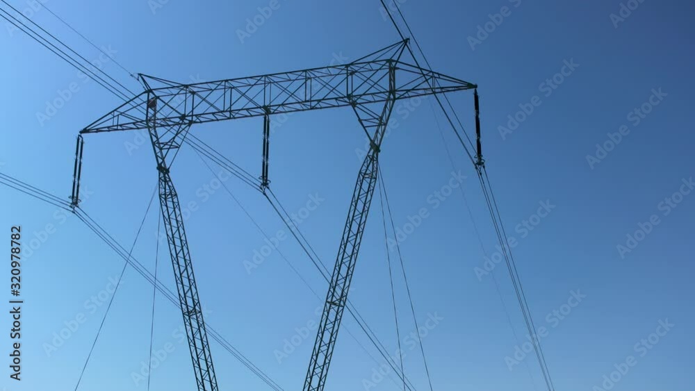 Looking up the electric lines on steel power pylon against blue sky - power industry or energy concept Looking up the electric lines on steel power pylon against blue sky - power industry or energy concept