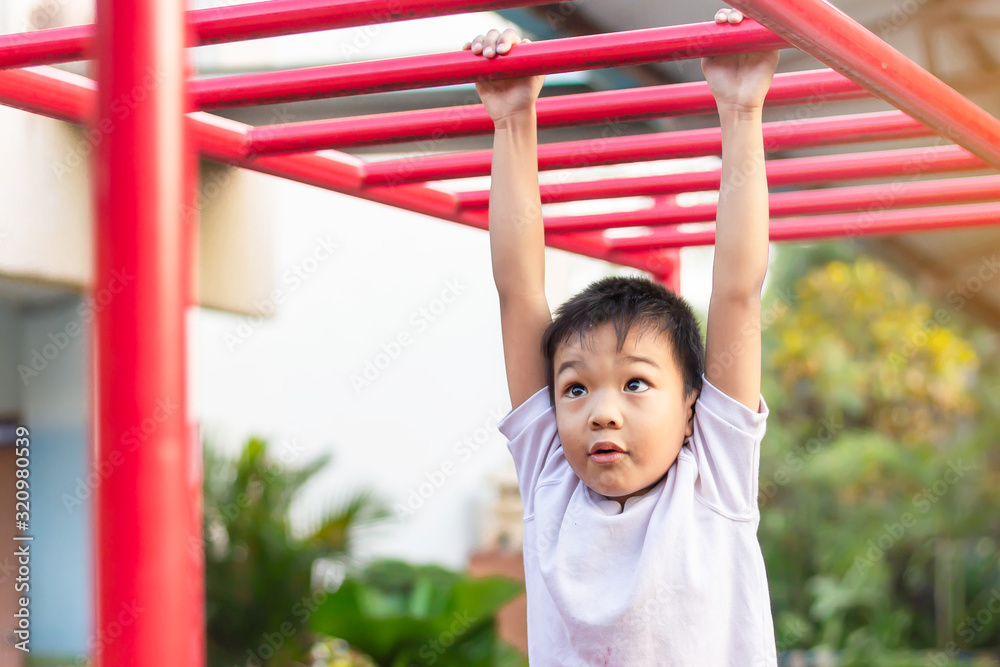 Kid exercise for health and sport concept. Happy Asian student child boy playing and hanging from a steel bar at the playground. 5-6 years old. Kid exercise for health and sport concept. Happy Asian student child boy playing and hanging from a steel bar at the playground. 5-6 years old.