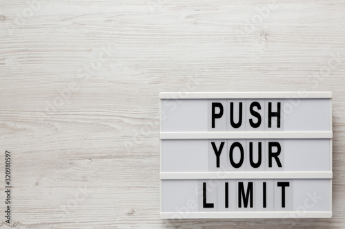 'Push your limit' words on a lightbox on a white wooden background, top view. Overhead, from above, flat lay. Copy space.