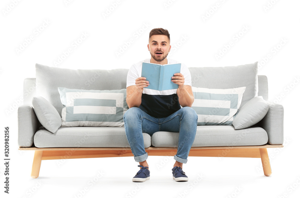 Young man reading book while sitting on sofa against white background Young man reading book while sitting on sofa against white background