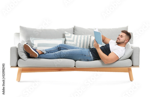 Young man with book lying on sofa against white background