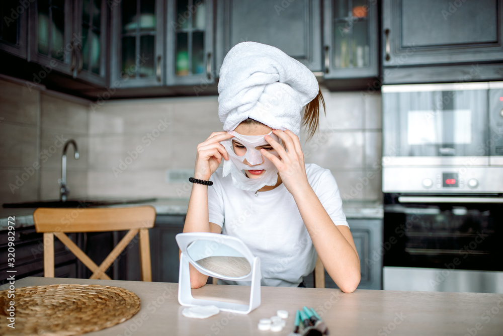 Girl shows a sign of class in a hygienic mask. Teenager and first skin care cosmetics. white mask at home in the kitchen Girl shows a sign of class in a hygienic mask. Teenager and first skin care cosmetics. white mask at home in the kitchen
