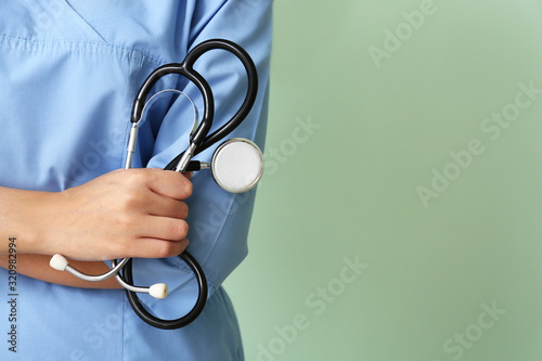 Young African-American nurse with stethoscope on color background, closeup photo