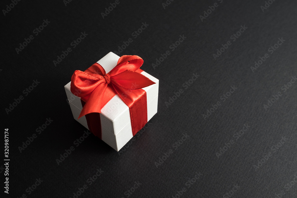 White gift box with red ribbon on dark black background.