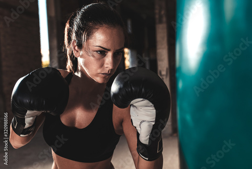Female boxer punching a boxing bag in warehouse. © Zoran Zeremski