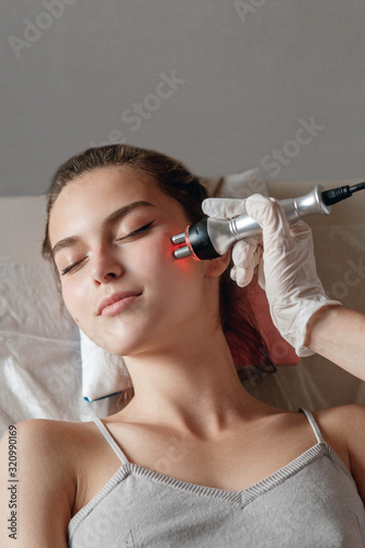 Hardware cosmetology. Picture of happy young woman with closed eyes getting rf lifting procedure in a beauty parlour.