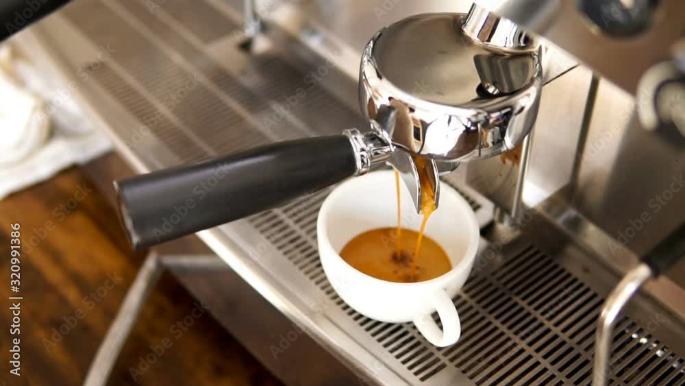 Coffee being brewed by the machine flowing through portafilter into the cup, slow motion shot