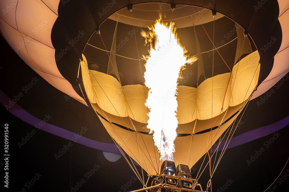 Obraz premium Preparation of a hot air balloon for flight by heating the air with a gas burner on evening in a summer day on a festival of ballooning