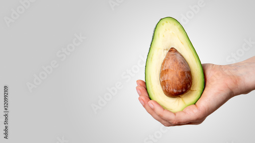 Avocado in hand on grey background. Vegetarian food and vitamins
