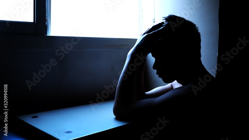 Depressed man silhouette sitting in a dark room. Mental health, depression and feeling blue concept