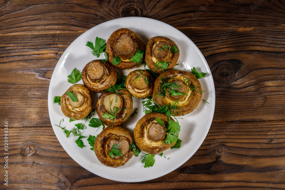 Baked mushrooms in plate on wooden table. Top view Baked mushrooms in plate on wooden table. Top view