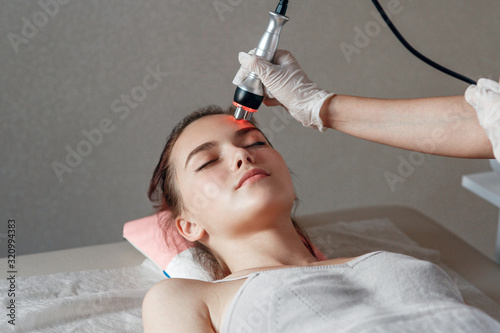 Hardware cosmetology. Picture of happy young woman with closed eyes getting rf lifting procedure in a beauty parlour.