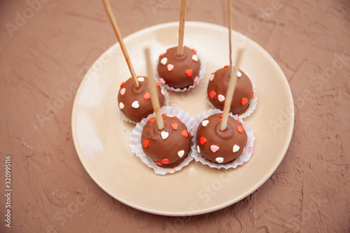 Chocolate candies covered with pink and red hearts on a stick lie on a white plate