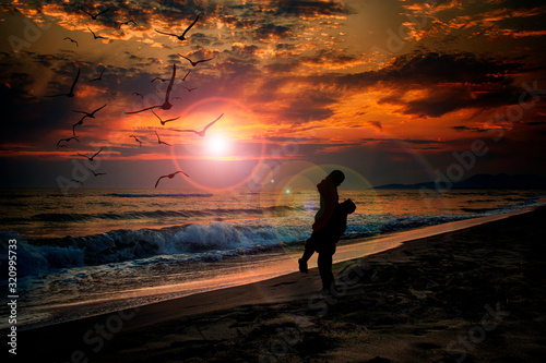 Silhouettes of a couple standing on a sandy beach with the sea and sunset in the background.