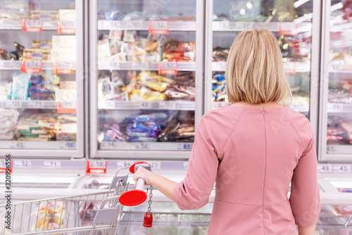 Young woman chooses frozen food in a supermarket.