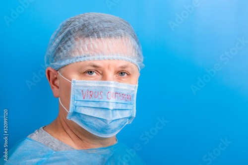 Portrait of man wearing medical uniform and mask with virus outbreak word at blue background. Protect your health. Coronavirus concept with copy space